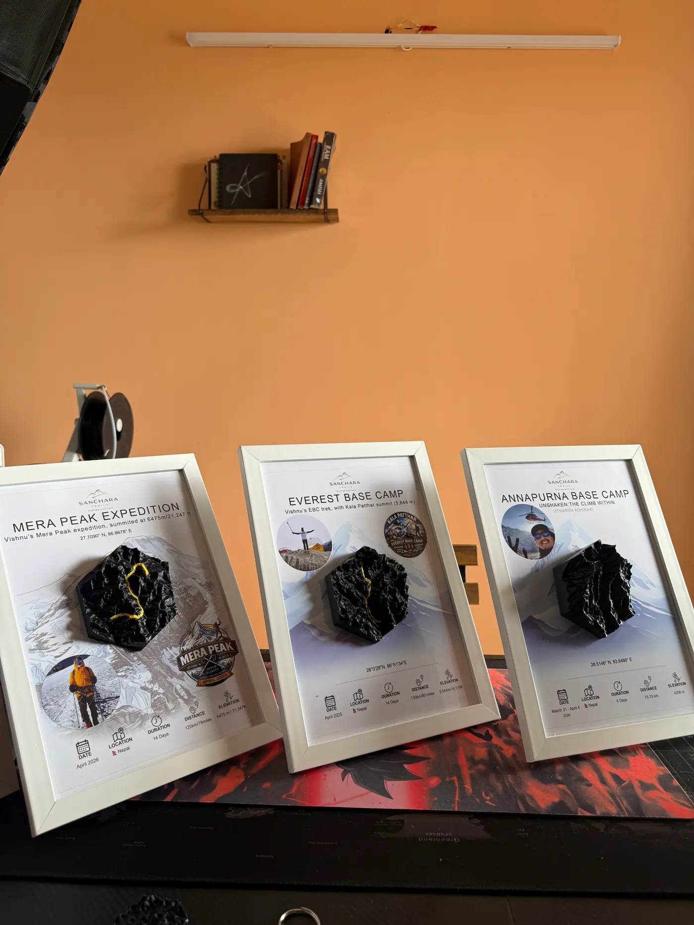 Three finished framed trail maps lined up on a shelf