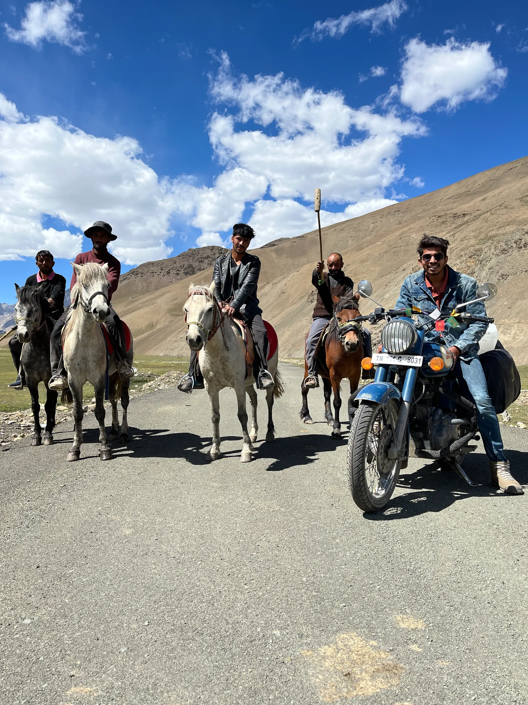 Aditya on a motorbike alongside horse riders on a high-altitude road